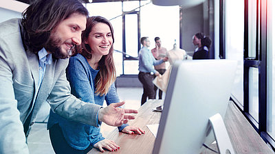Frau und Mann lachend vor PC-Bildschirm in modernem Büro
